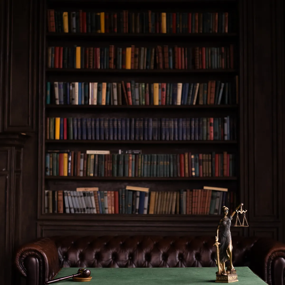 Biblioteca jurídica del estudio con sillón de cuero y una figura de la justicia sobre la mesa